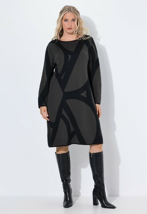 Langärmliges Strickkleid in Dunkelgrau mit schwarzem abstraktem Design. Mit einem gerundeten Ausschnitt und einer lockeren Passform, kombiniert mit schwarzen kniehohen Boots.