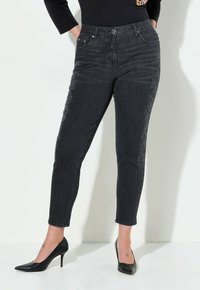 Jeans de mezclilla negra con un diseño ajustado, que presentan rhinestones decorativos en el costado y una cintura de media altura. Combinados con tacones altos negros.