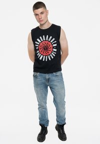 Black sleeveless T-shirt featuring red graphic print with circular design, paired with light blue denim jeans and black lace-up boots.
