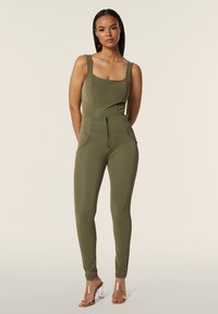 Body verde oliva con spalline larghe, scollatura quadrata e dettaglio con zip in vita; design aderente. Sandali con tacco trasparente.