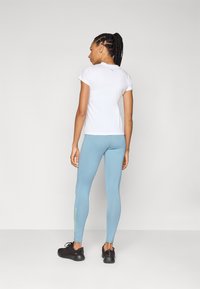 Hvit kortermet topp og lyseblå leggings med en tettsittende design. Sorte treningssko. Logodetaljer i lyseblått og grønt på leggingsene.