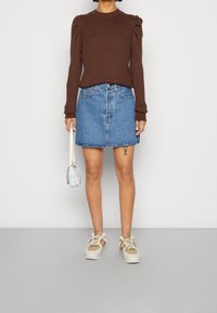 Brauner, gerippter Strickpullover mit puffigen Ärmeln, kombiniert mit einem hellblauen Jeansrock, beigen und weißen Sneakern und einer kleinen, gemusterten Handtasche.