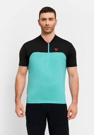 Mann trägt ein kurzärmliges schwarzes und türkisfarbenes Sportshirt mit halbem Reißverschluss und kleinem roten Logo auf der Brust, steht vor einem schlichten weißen Hintergrund.