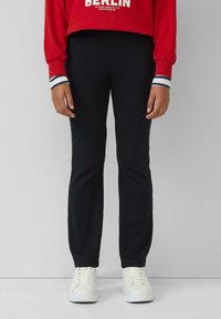 Pantaloni da jogging neri a coste con una vestibilità slim, dotati di una vita elasticizzata e cuciture laterali. Abbinati a sneaker bianche su uno sfondo neutro.