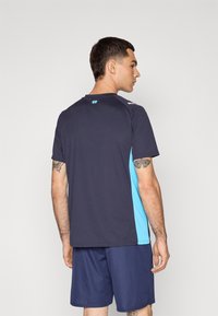 T-shirt atlético de azul marinho escuro com painéis laterais em azul claro, mangas curtas, gola redonda e detalhe do logótipo nas costas; combinado com calções azuis marinhos.