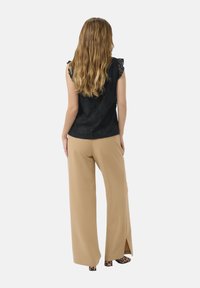 Črna čipkasta majica z nabranimi rameni, kombinirana s svetlečimi širokimi hlačami z razporki. Obutev s potiskom dopolnjuje videz.