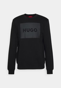 Sudadera negra con mangas largas, cuello redondo, con un logo rectangular negro mate "HUGO" en el centro. Tejido suave, puños acanalados.