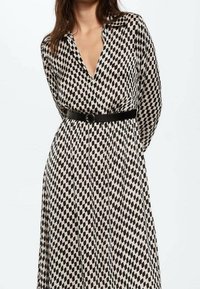 Vestido largo de estampado blanco y negro con escote en V, mangas largas y un cinturón negro que acentúa la cintura. Tela suave y fluida.