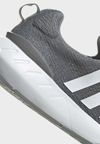 Grey Adidas sneaker with textured knit upper, white midsole, three white stripes, and heel pull loop for easy wear.
