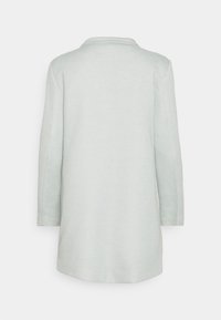 Ljusgrå kappa med långa ärmar, kilkrage, midjelång design och ett texturerat tyg. Inga synliga knäppningar eller detaljer.