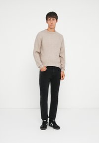 Suéter de punto beige claro, jeans negros y zapatillas negras con acentos blancos. Diseño sencillo, cuello redondo y silueta ajustada.