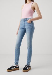 Ljusblå skinny jeans med blekningar, ihopparat med en rosa ribbad linne och svarta sneakers med vita ränder och gummisulor.