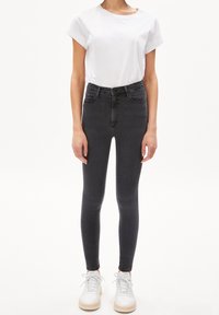 Tmavě šedé skinny džíny vyrobené z denimu, s vysokým pasem, pěti kapsami a hladkou texturou. Kombinované s bílým tričkem a bílými teniskami.