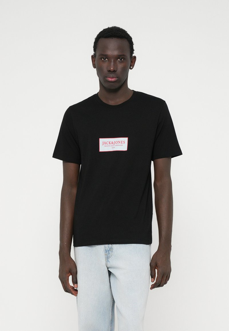 Μαύρο βαμβακερό μπλουζάκι με ορθογώνιο κόκκινο και λευκό λογότυπο στο μπροστινό μέρος. Κοντά μανίκια και κλασικός σχέδιο στρογγυλής λαιμόκοψη.