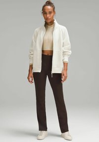 Valkoinen vetoketjullinen huppari, jossa on korkea kaulus, beige lyhythihainen toppi alla ja ruskeat istuvat housut, yhdistettynä valkoisiin lenkkikenkiin. Pehmeä kangas.