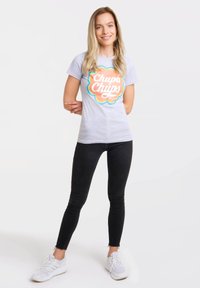 Light gray t-shirt with "Chupa Chups" logo in orange and blue; paired with black jeans and white athletic shoes. Smooth texture, fitted design.