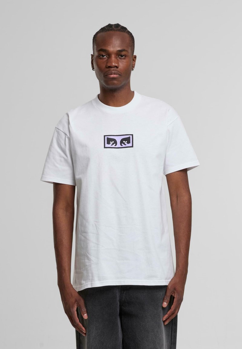 Hvid bomulds t-shirt med et centralt sort og lilla grafisk design. Korte ærmer, rund hals, afslappet pasform, ingen synlige mønstre.