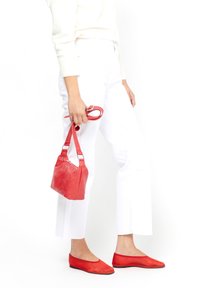 Borsa a tracolla rossa in pelle con finitura texturizzata, manici corti e tracolla rimovibile. Indossata con pantaloni bianchi e ballerine rosse abbinate.