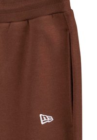 Brune joggebukser laget av et mykt materiale, med ribbet liv og sidelommer. Diskret hvit logo brodert på nederste ben.