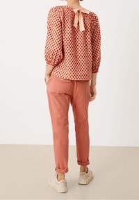 Rød og hvid mønstret bluse med en båndlukning bagpå, parret med lyserøde bukser og beige sneakers, der viser et afslappet outfitdesign.