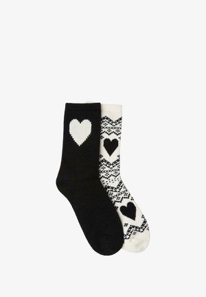 Calzini in bianco e nero, uno completamente nero con un cuore bianco, l'altro bianco con un cuore nero e motivi geometrici. Materiale in misto cotone.