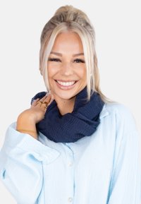 Écharpe infini texturée bleu marine en tissu doux, portée sur une chemise à boutons bleu clair froissée, créant un style superposé.