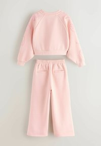 Jasnoróżowy sweter z raglanowymi rękawami i nadrukowanymi akcentami, w połączeniu z pasującymi spodniami o szerokich nogawkach, z elastycznym pasem i tylnymi kieszeniami.