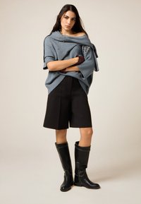 Överdimensionerad blå stickad tröja med detaljer, svarta skräddarsydda shorts och svarta knähöga läderstövlar med vita sömmar.