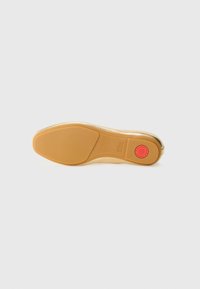 Light gold shoe sole with a smooth texture, oval shape, and a red circular accent near the heel. Rubber bottom with grip pattern.