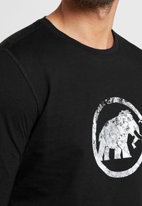 Czarna bawełniana koszulka z długim rękawem z teksturowanym białym wzorem słonia w owalnym kształcie, okrągły dekolt i widoczne detale przeszycia.