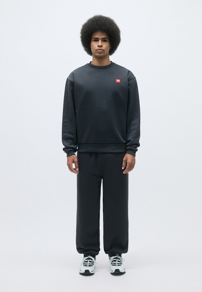 Sudadera gris oscuro y pantalones a juego hechos de una tela suave, con un pequeño detalle de logo rojo en el pecho y en el lado de los pantalones.