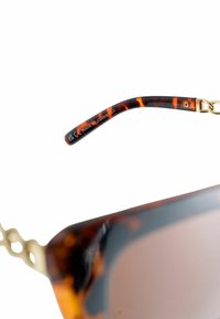 Teknőspáncél napszemüveg fényes kivitelben, aranyszínű részletekkel a szárnál és enyhén tónusos lencsékkel. Látható a "Made in China" felirat.