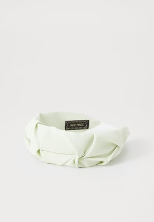 Fascia in tessuto verde con un design attorcigliato, caratterizzata da una texture liscia e un leggero lucido, etichettata "FATTO A MANO" su un piccolo tag.
