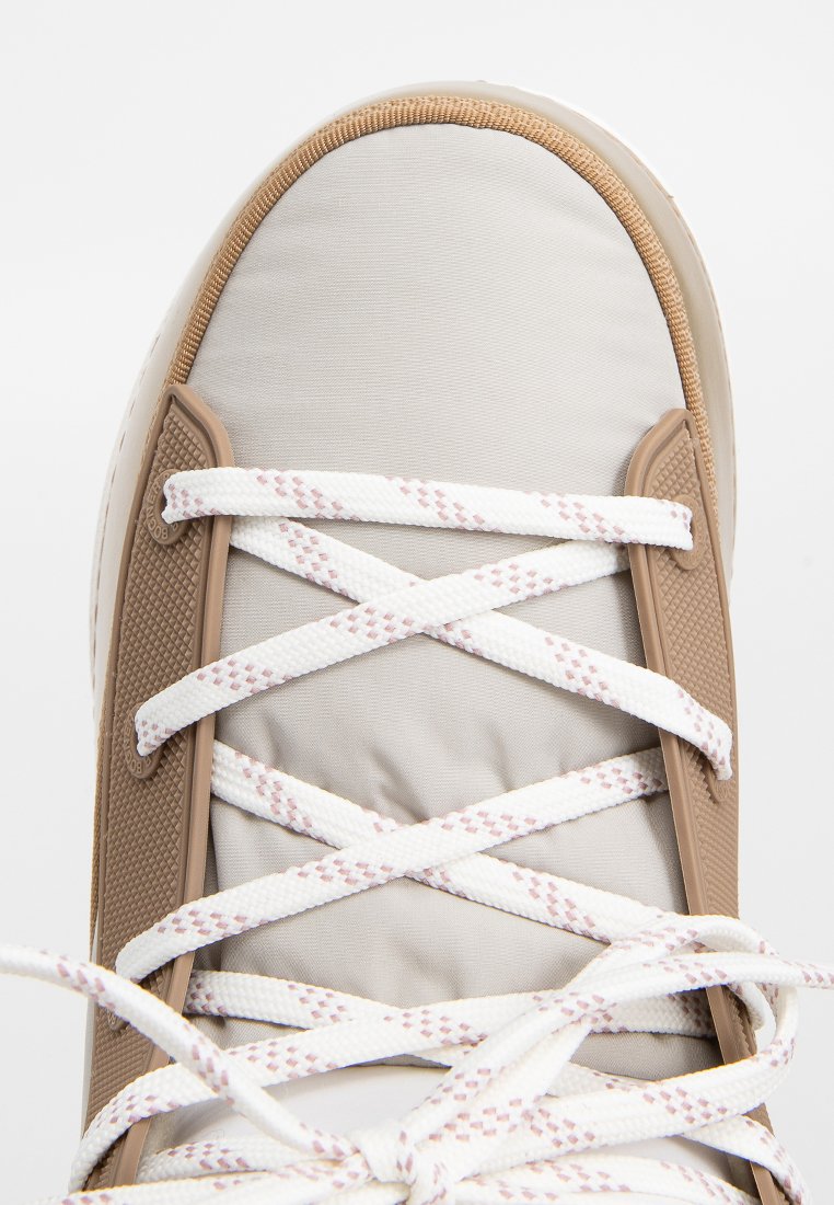 Sneaker beige chiaro con parte superiore imbottita, caratterizzato da lacci bianchi e dettagli marrone chiaro. Suola in gomma testurizzata e cuciture decorate.