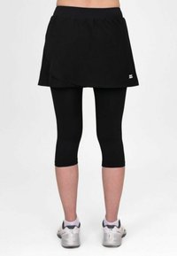 Falda atlética negra sobre mallas negras, con un diseño en capas. La tela parece suave, con una cintura elástica y un branding mínimo.