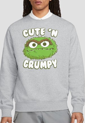 Gray sweatshirt featuring a green, furry character with large white eyes and brown eyebrows. Text reads "CUTE 'N GRUMPY" below the character.