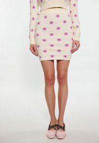 Strick-Minirock in Creme mit pinken und lila Blumenmustern. Kombiniert mit hellpinkfarbenen Schuhen, die schwarze Riemen und silberne Hardware-Akzente haben.