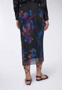 Gonna nera floreale con una trama trasparente, caratterizzata da vivaci motivi di fiori blu, viola e arancioni. Design a lunghezza media, indossata con sandali neri con cinturini.