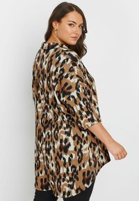 Blusa marrone con stampa leopardata, maniche 3/4, tessuto leggero e orlo curvo, caratterizzata da diverse tonalità di marrone, nero e crema.