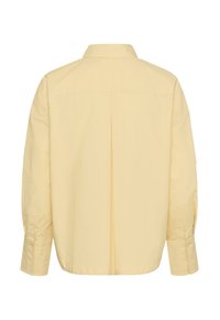 Světle žlutá košile s dlouhým rukávem na knoflíky, s límečkem sklopeným dolů, zobrazena zezadu s centrálním skladem a zapnutými manžetami.