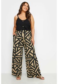 Top de tirantes negro acanalado con botones, combinado con pantalones de pierna ancha que presentan un patrón geométrico en negro y beige. Tejido ligero.