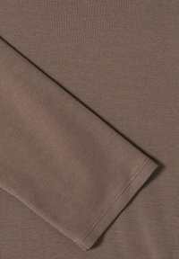 Tissu marron à manches longues présentant une texture lisse et un poignet côtelé. Le matériau semble doux et légèrement extensible. Un détail de couture propre est visible.