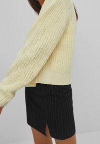 Jasnożółty sweter z dzianiny o fakturowanym wzorze, zestawiony z czarną mini-spódnicą w pionowe prążki z bocznym rozcięciem.