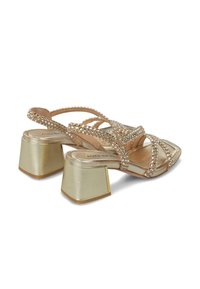 Sandalias de tacón alto con tiras que presentan una base nude, un tacón bloque dorado y adornos de strass transparente a lo largo de las tiras.