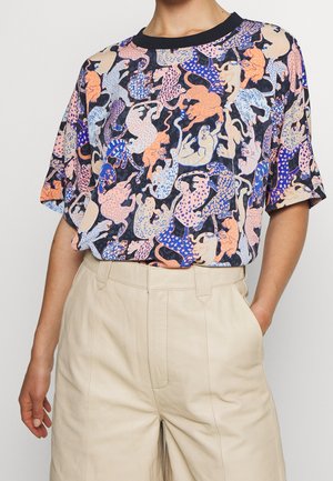 T-shirt with colorful abstract leopard print in blue, orange, pink, and beige, paired with high-waisted beige pants.