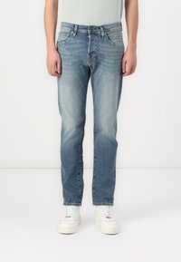 Jeans din denim de un albastru deschis, cu un design cu picior drept, zone decolorate, stil cu cinci buzunare și închidere cu nasture, asortați cu adidași albi.