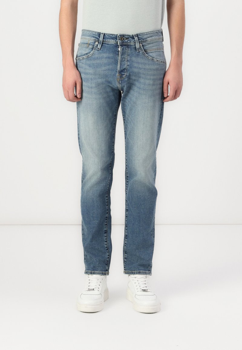 Jeans din denim de un albastru deschis, cu un design cu picior drept, zone decolorate, stil cu cinci buzunare și închidere cu nasture, asortați cu adidași albi.