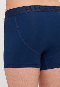 Boxers bleu marine avec une taille élastique douce arborant "HILFIGER" en texte noir. Texture lisse avec des détails de couture contrastés.