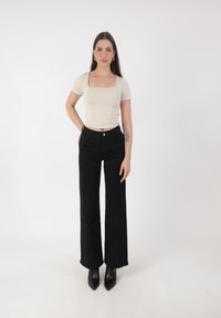 Beige top met vierkante hals, gecombineerd met hooggesneden zwarte wijde broek met verticale glinsterlijnen. Model draagt zwarte puntige enkellaarsjes.