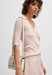 Maglione a coste rosa con scollo a V e maniche corte, abbinato a una borsa bianca con hardware dorato e tracolla.